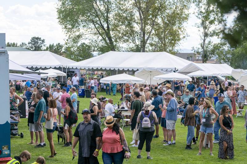 Groups of people mill about on a lawn with white tents and food trucks at Sedona WineFest.